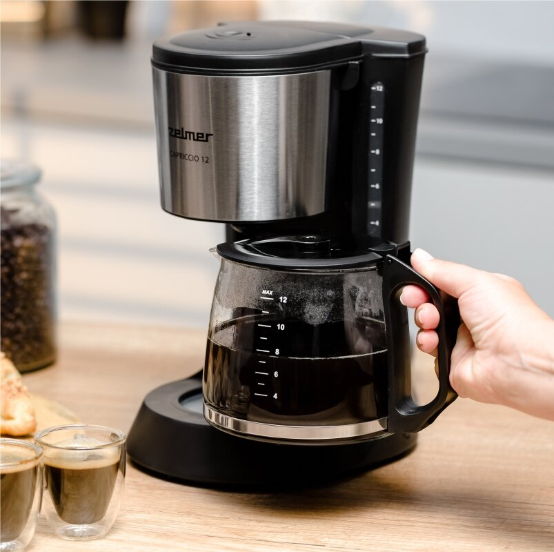 Ręka trzyma dzbanek ekspresu do kawy wypełniony kawą.