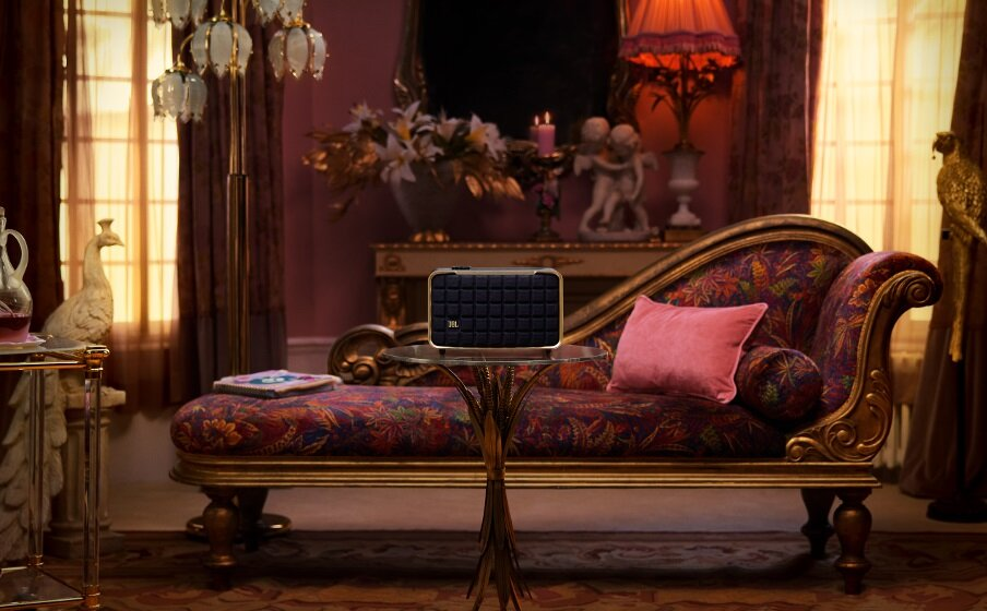 Pokój w stylu retro z głośnikiem na stole, leżanką i elementami dekoracyjnymi.