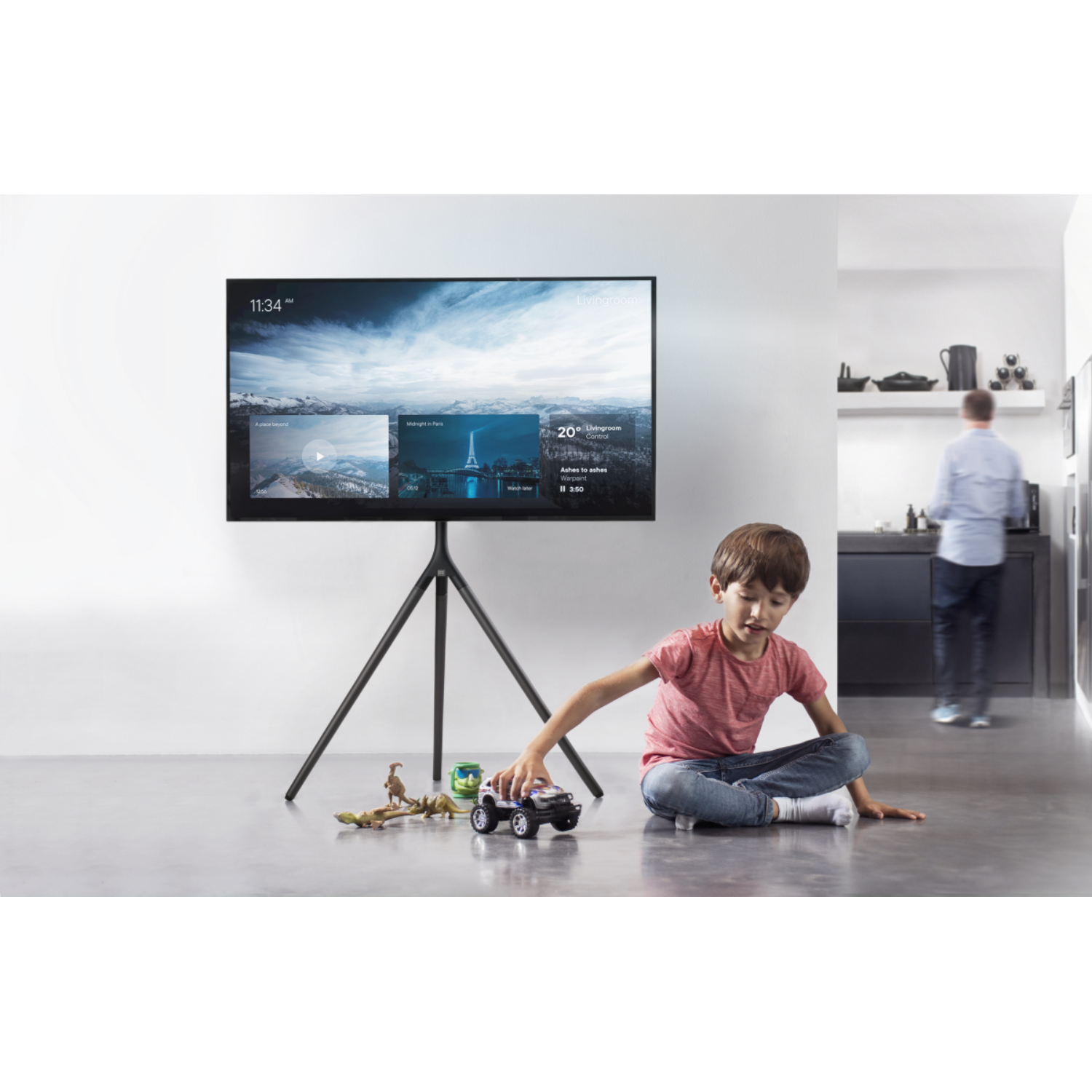 Boy playing with toy cars in front of a TV with a black tripod stand.