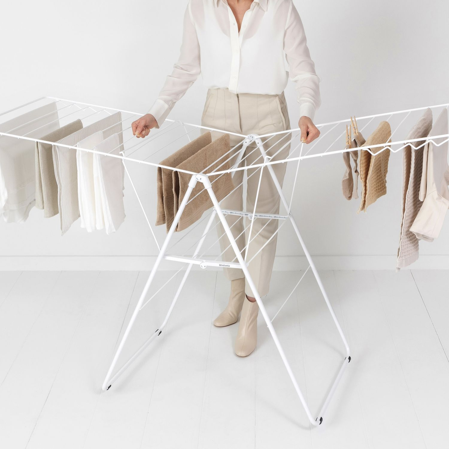 Een vrouw staat bij een witte droogmolen met hangende kleding, tegen een witte muur en vloer.