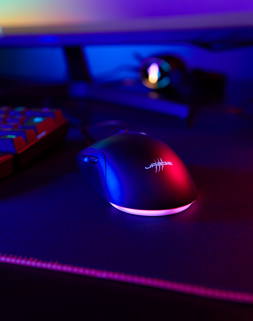 Fekete gamer egér világító talppal, fekete felületen, billentyűzet és monitor közelében.