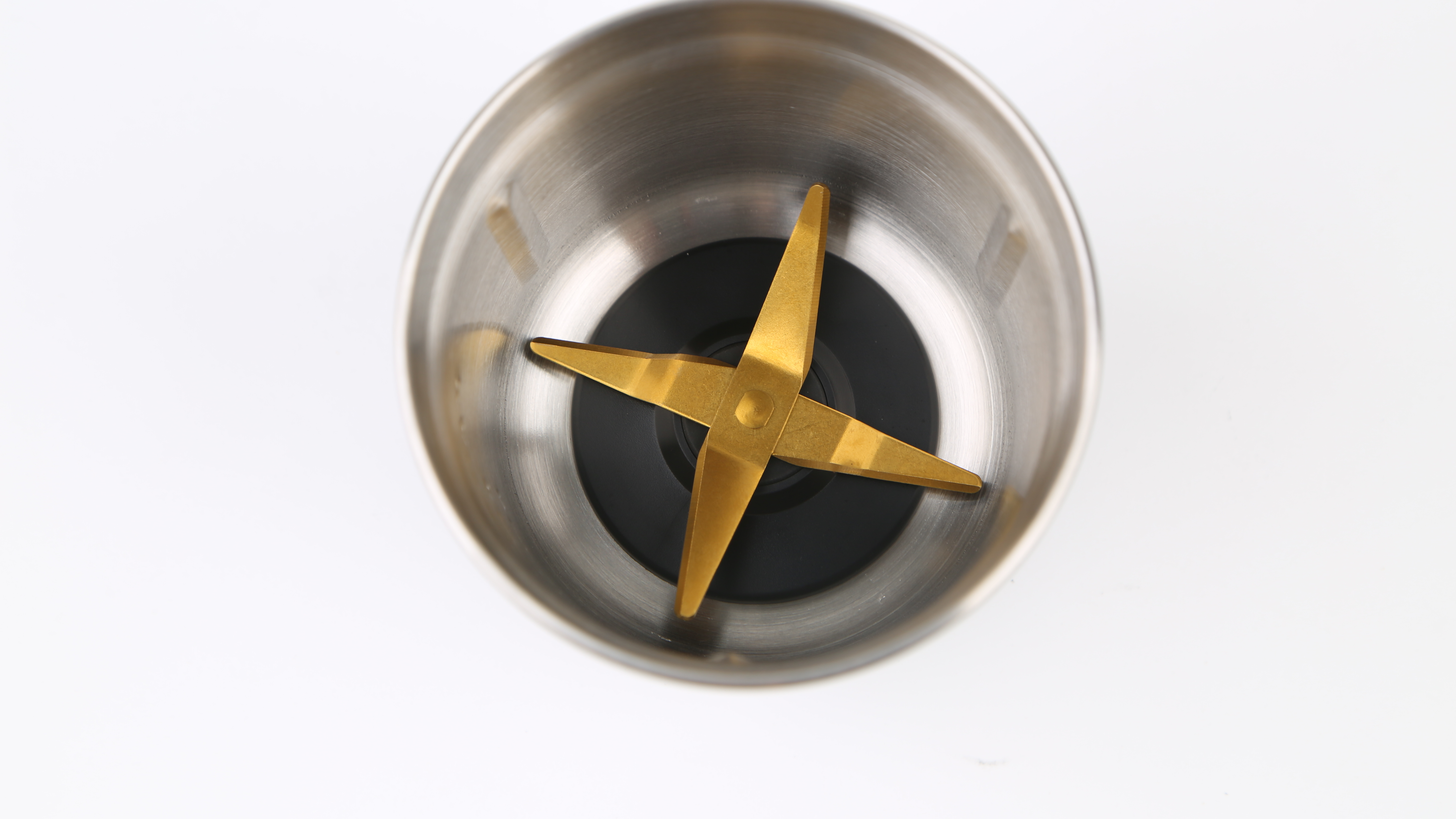 Metallschüssel eines Mixers mit goldenen Klingen, vor weißem Hintergrund.