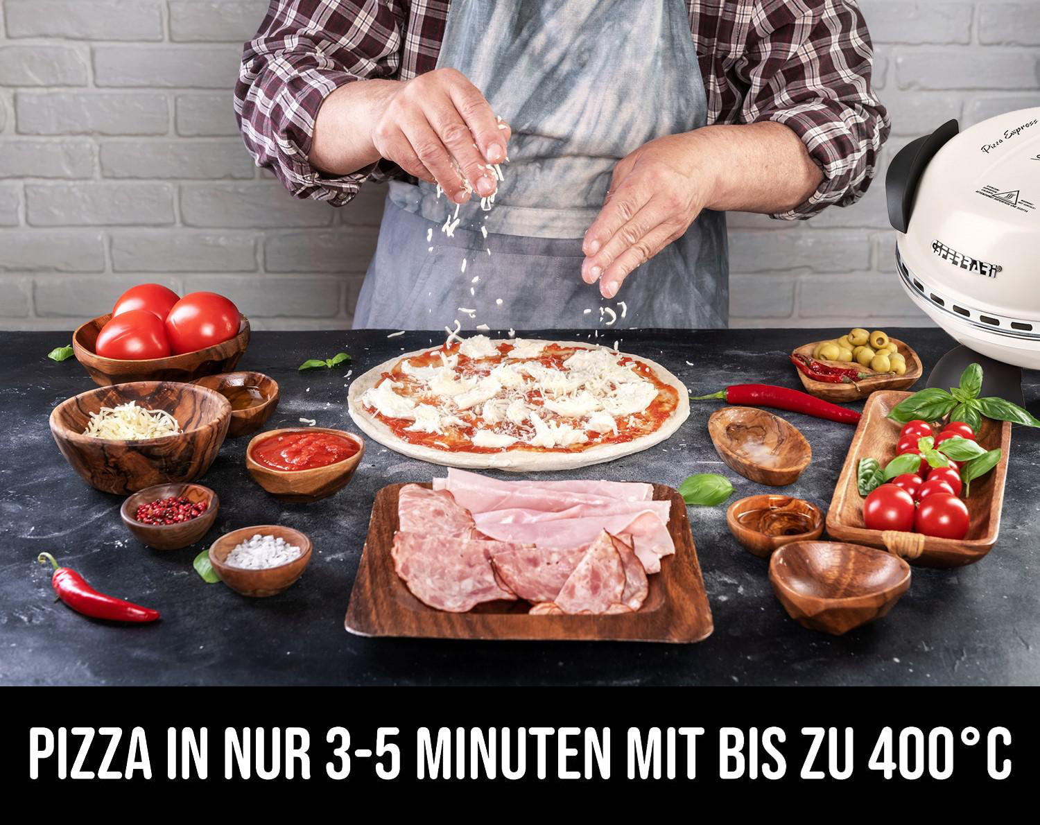 Pizza mit Belag wird zubereitet. Tomaten, Schinken, Käse, Oliven in Holzschalen auf schwarzem Tisch.
