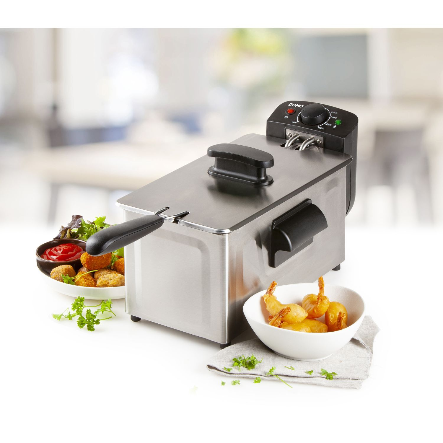Rvs friteuse met gefrituurd voedsel, ketchup en peterselie op een wit oppervlak.