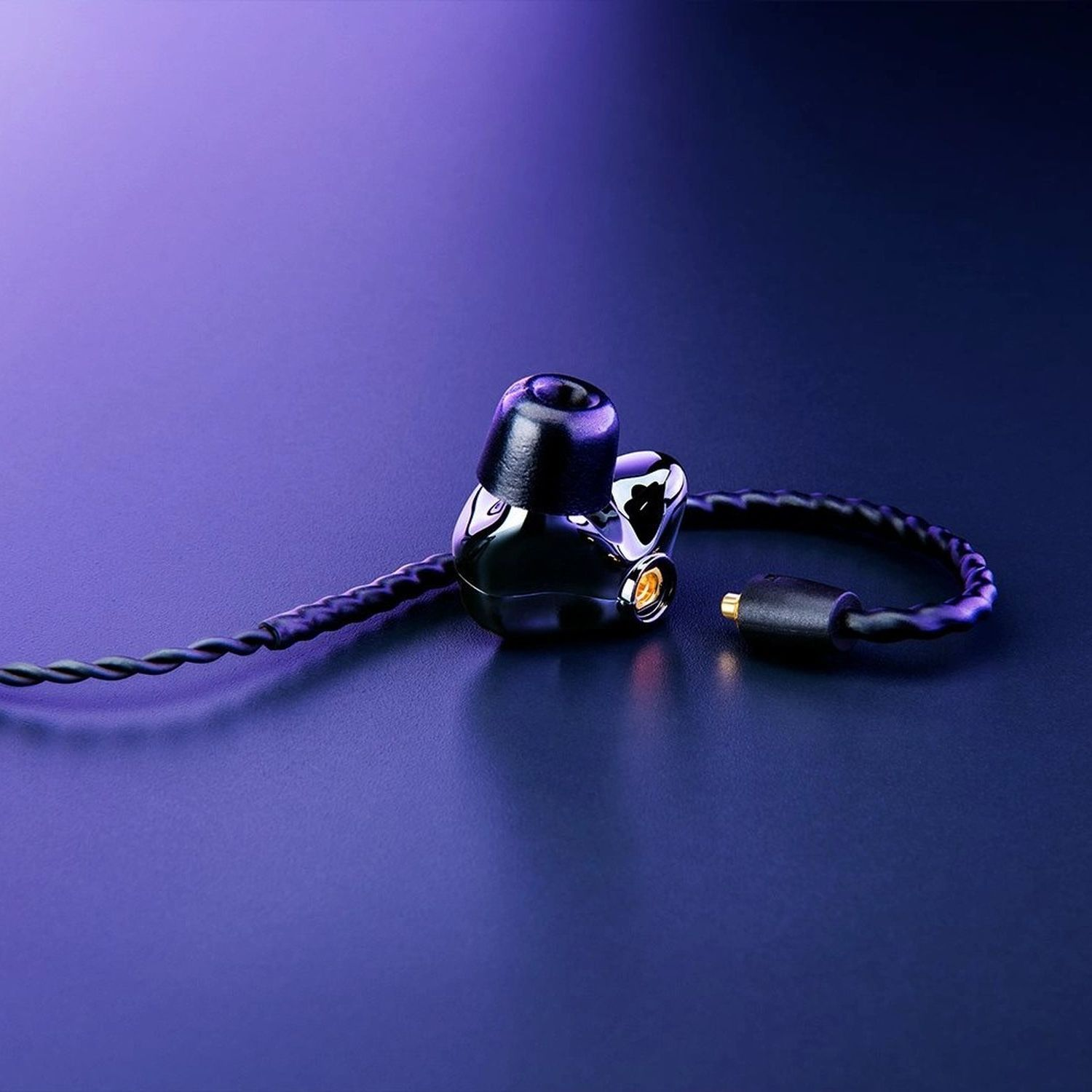 Zwarte in-ear koptelefoon met een kabel en een goudkleurige connector, op een paars oppervlak.