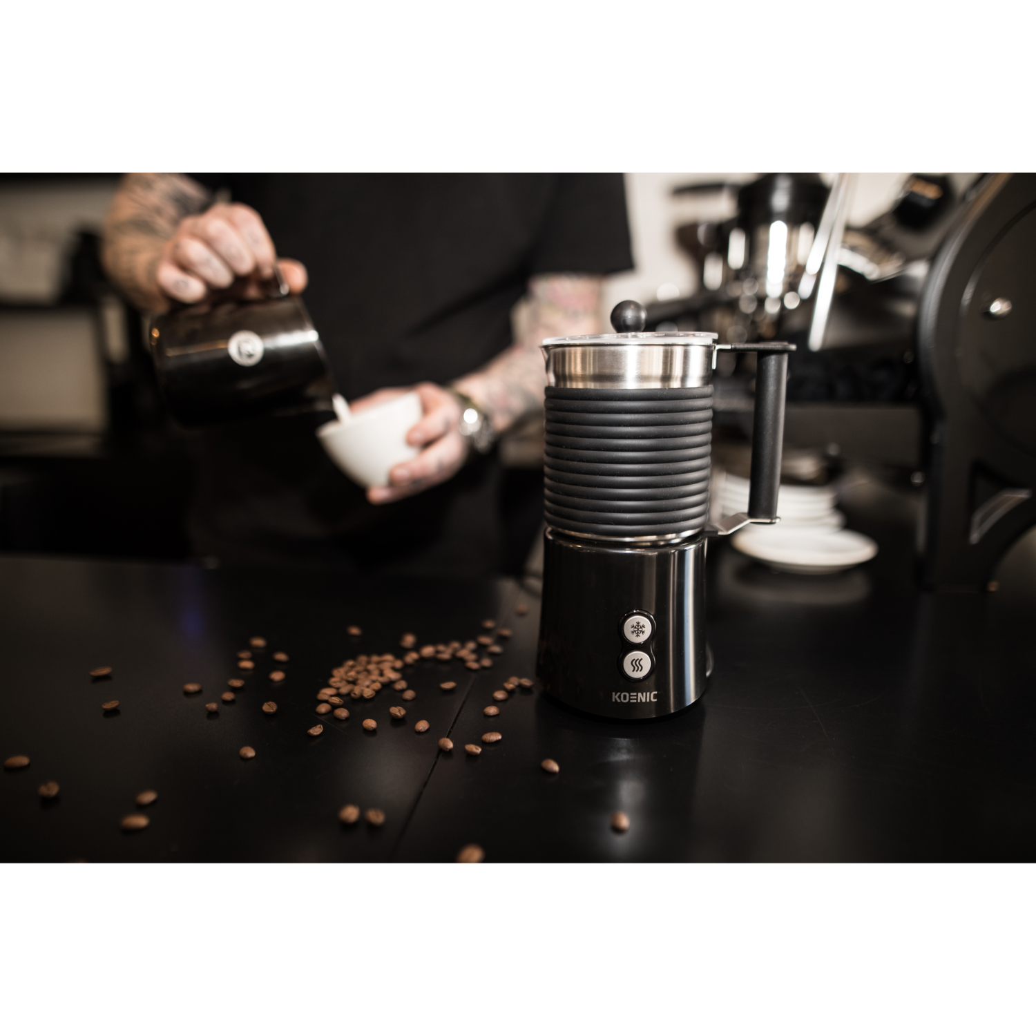 A person pouring milk into a cup, with a coffee machine and coffee beans on the counter.