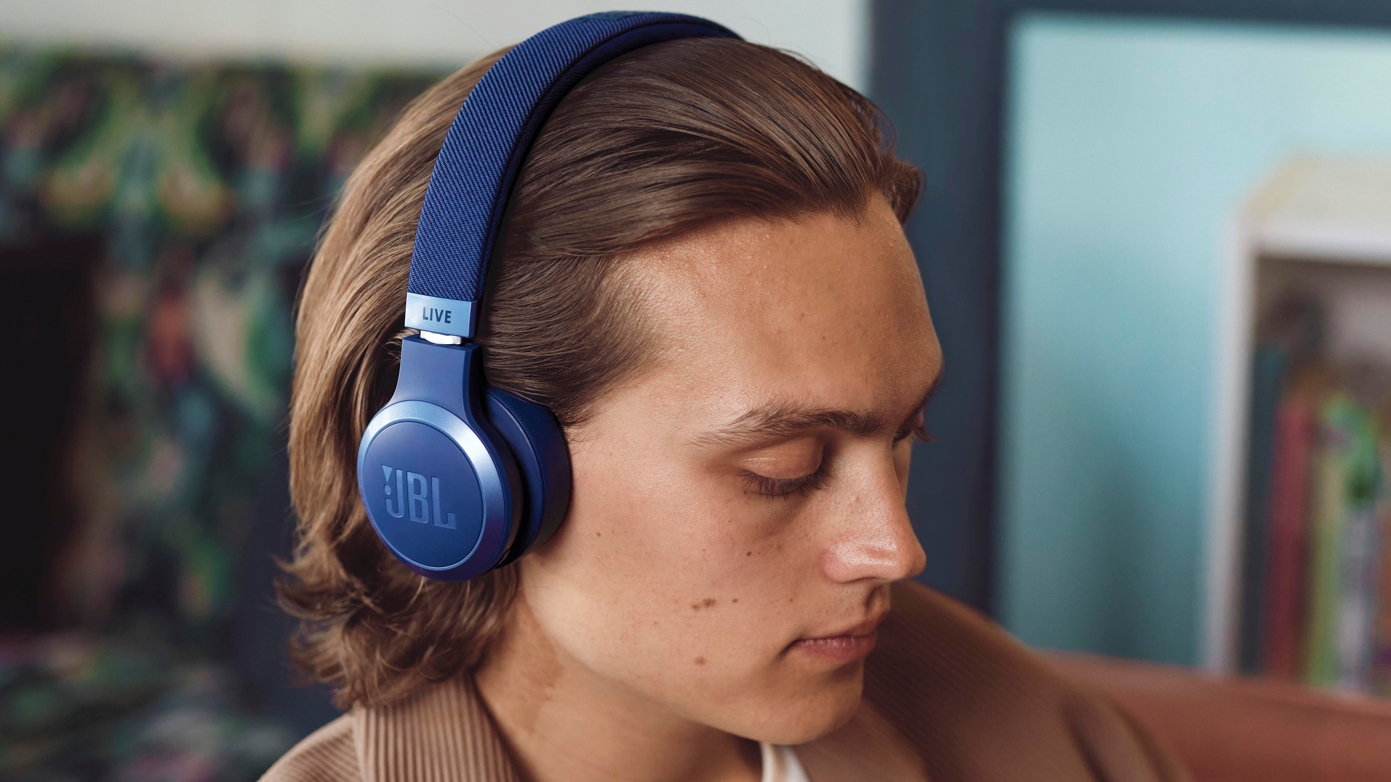 Ein Mann mit blauen JBL-Kopfhörern. Er hat helle Haut und braune Haare. Der Hintergrund ist unscharf.