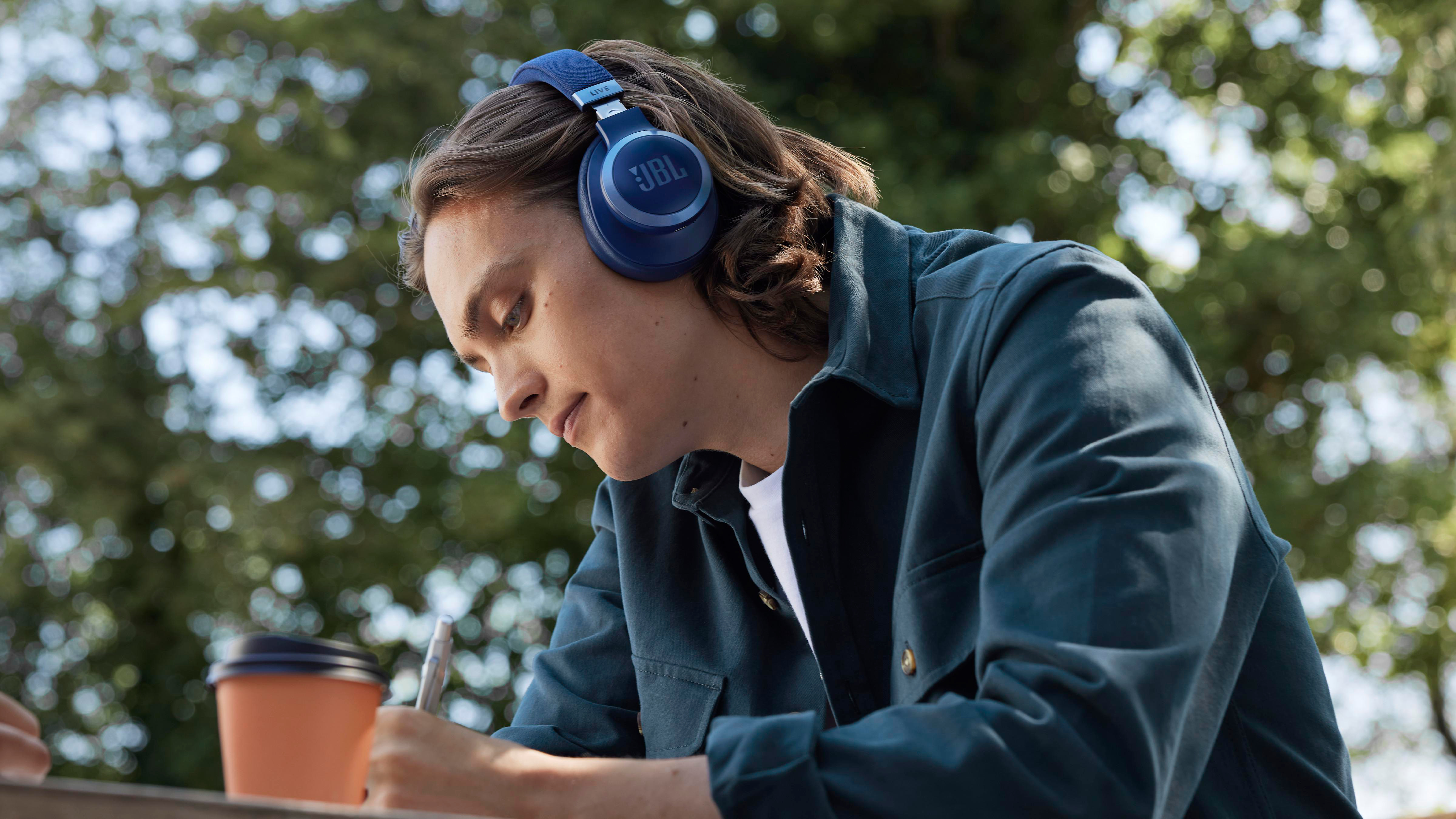 Eine Person mit blauen JBL-Kopfhörern schreibt draußen in ein Notizbuch.