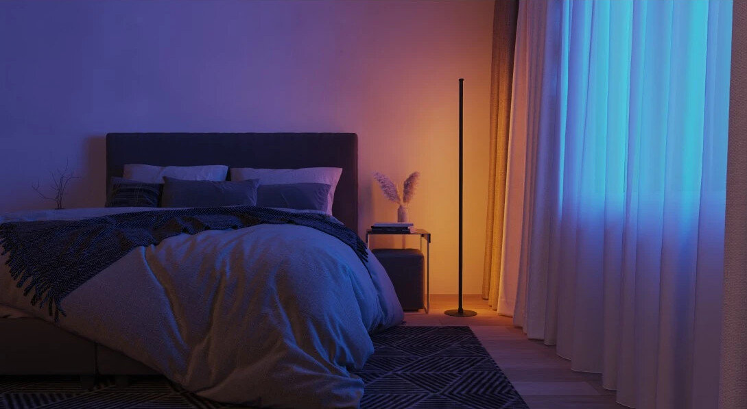 Sypialnia z niebieskim i pomarańczowym oświetleniem otoczenia, łóżko, dywan i lampa podłogowa.