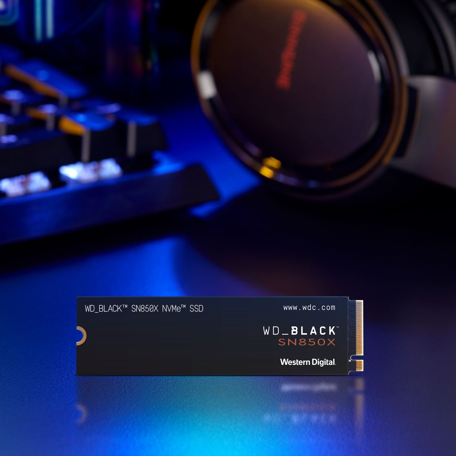 WD_BLACK SN850X NVMe SSD op een blauw oppervlak, met hoofdtelefoon en toetsenbord op de achtergrond.