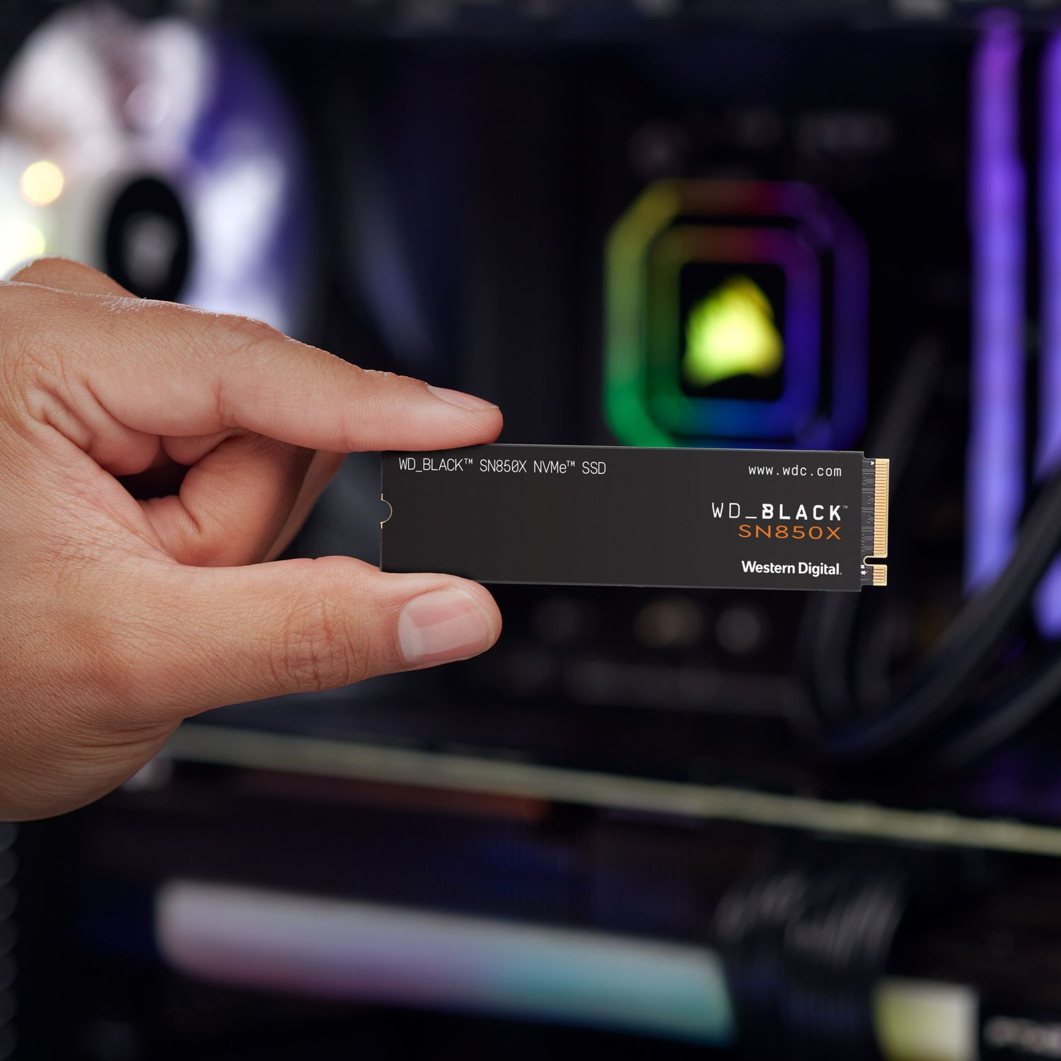 Een hand die een zwarte WD_BLACK SN850X NVMe SSD vasthoudt, met een computer op de achtergrond.