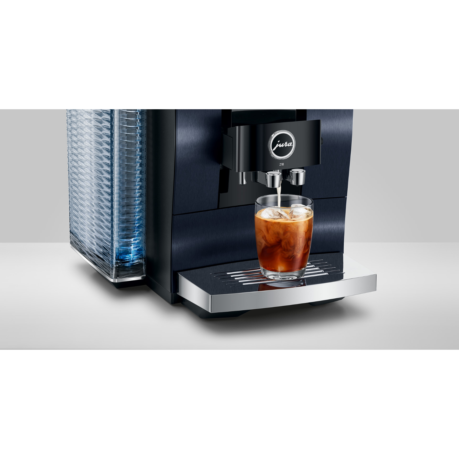 Jura coffee machine dispensing coffee into a glass with ice. Cups sit to the left.