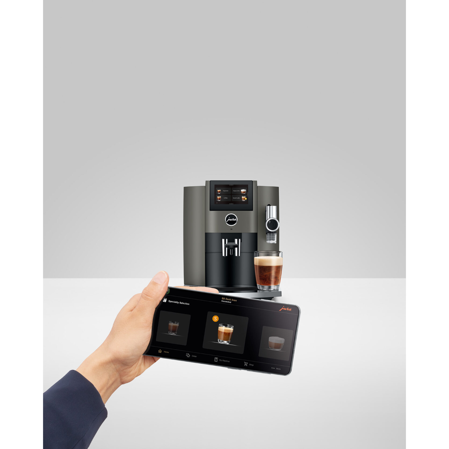 A person is holding a tablet, showing a coffee machine with a coffee cup next to it.