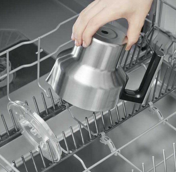 Ręka umieszczająca metalową pokrywę w zmywarce. Obraz jest zrobiony z góry.