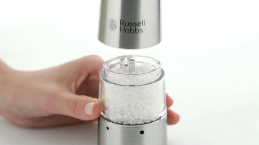 Ręka odkręca górę młynka do soli, odsłaniając gruboziarnistą sól w środku.