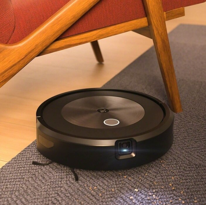 Czarny odkurzacz iRobot Roomba na szarej macie w pobliżu krzesła.