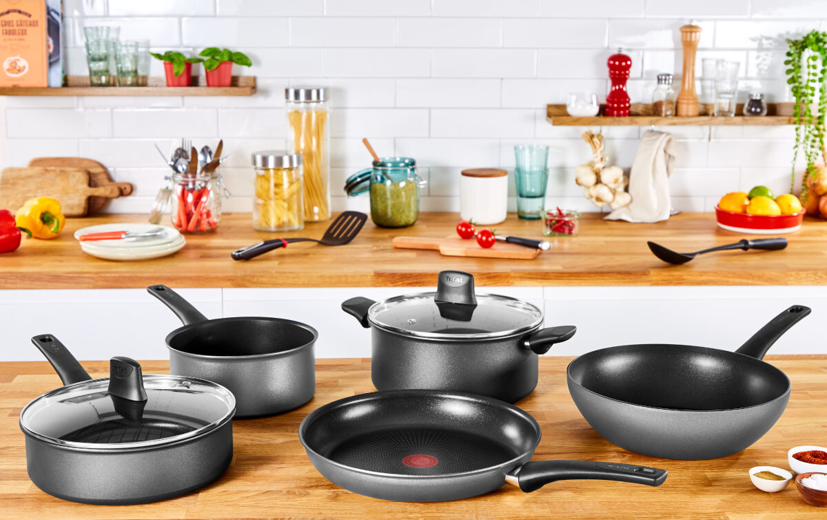 Scena kuchenna z naczyniami kuchennymi na drewnianym blacie. Wystawione są garnki, patelnie i przybory kuchenne.