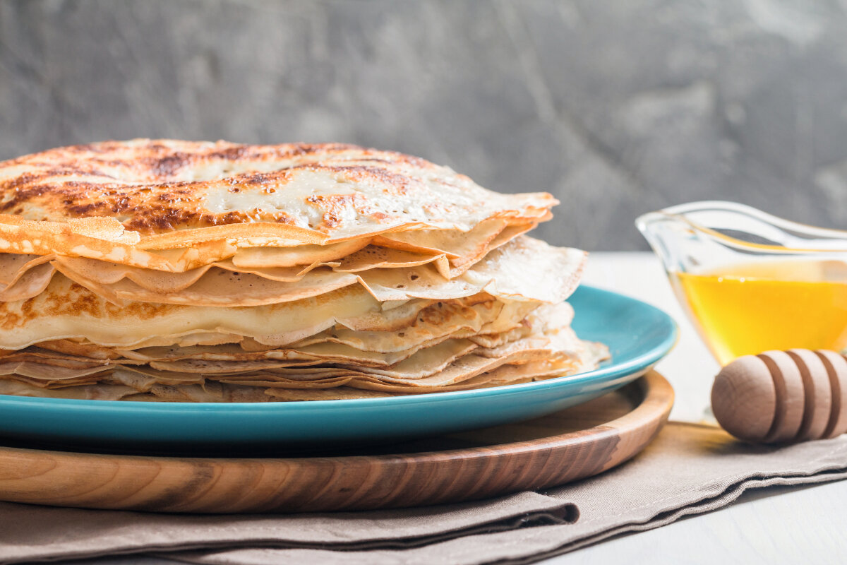 Stos naleśników na niebieskim talerzu, z miodem i nabierakiem do miodu w pobliżu.