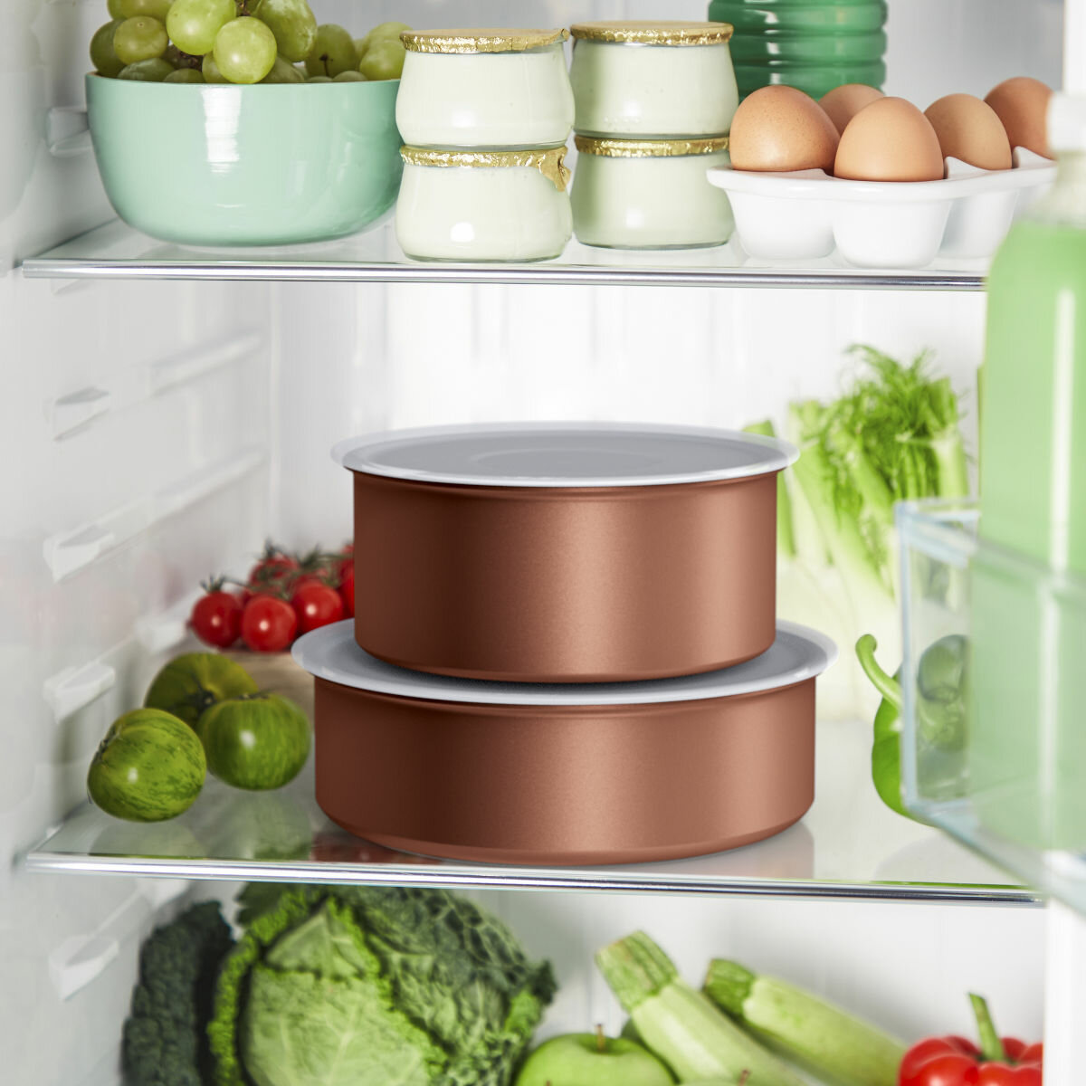 Półki lodówki wypełnione jedzeniem: produkty, pojemniki z nabiałem i jajka w kartonie.