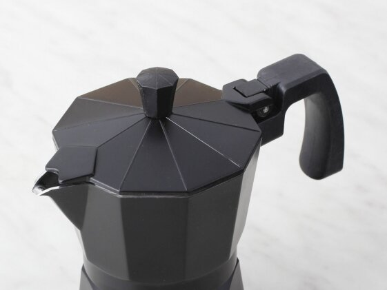 Czarny ekspres do kawy, widok z góry. Pokrywa jest otwarta. Stoi na białej powierzchni.