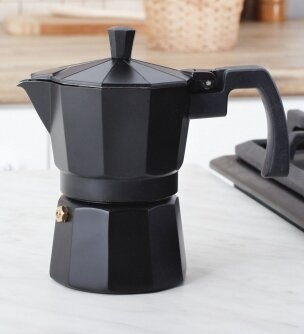 Czarny ekspres do kawy na blacie. Obok kuchenki gazowej, na białej powierzchni.