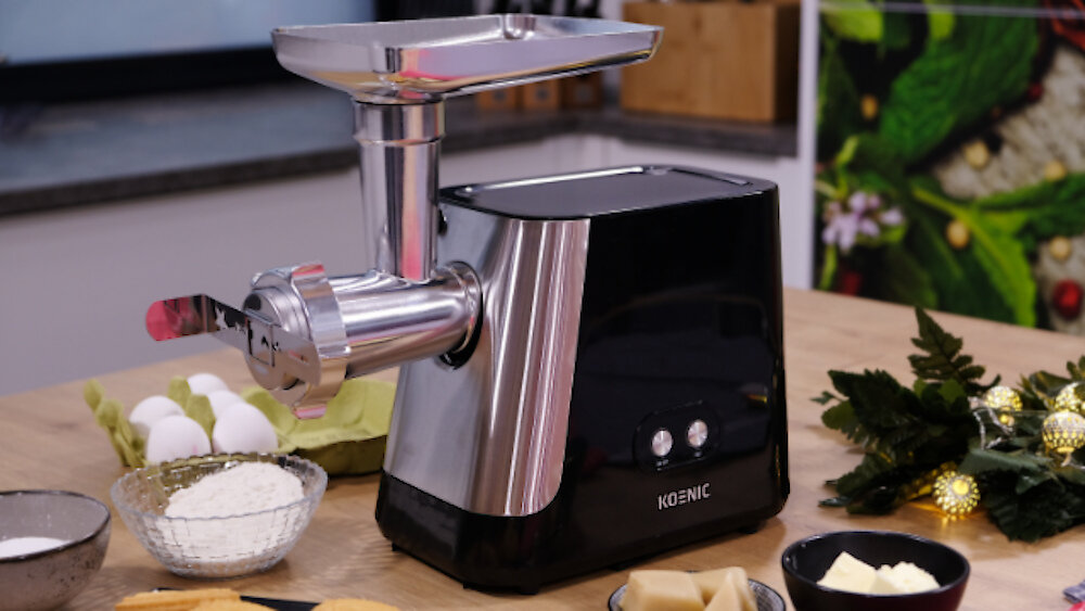 Maszynka do mięsa ze składnikami takimi jak jajka i mąka na drewnianym stole. Obecne są również masło i inne przedmioty.