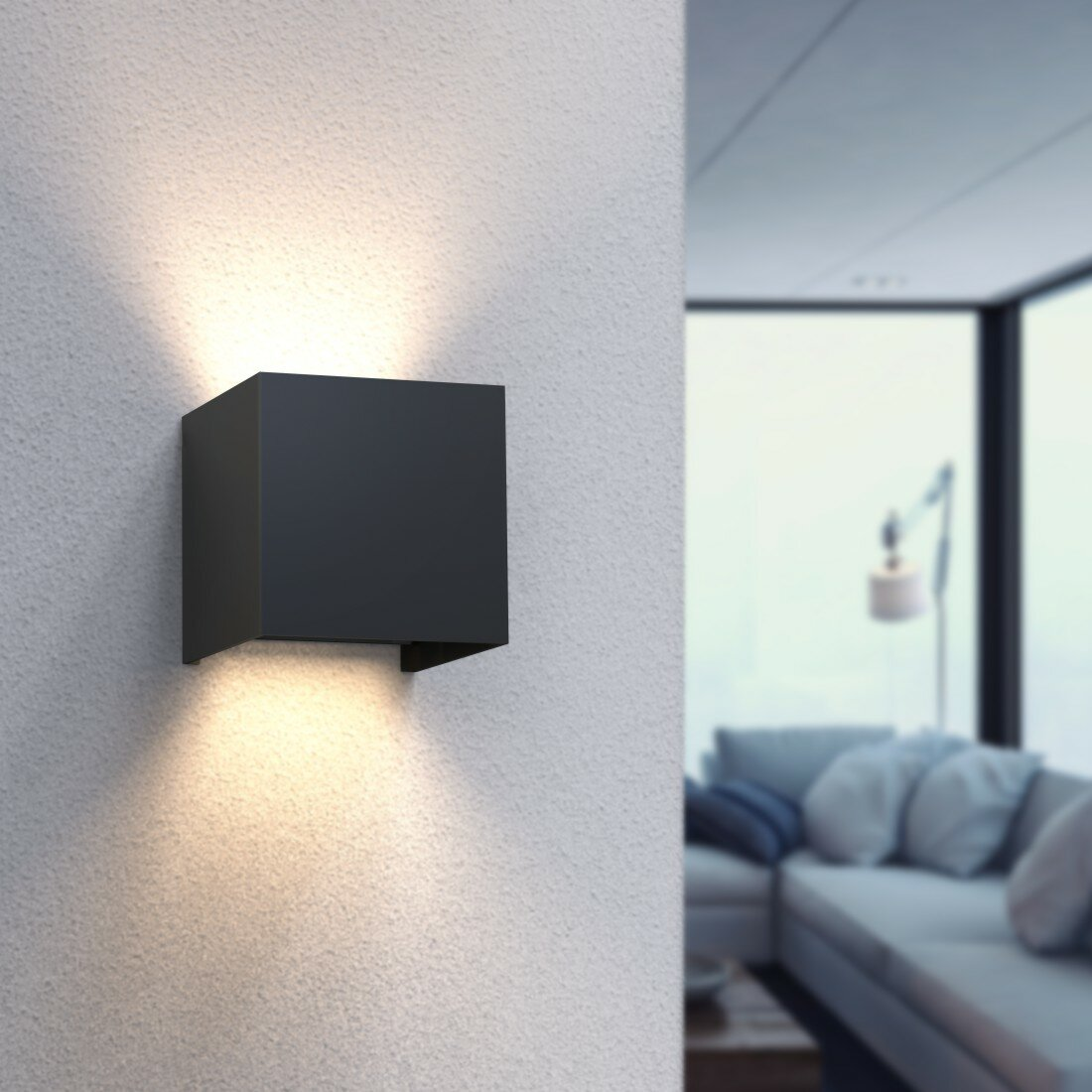 Czarna kwadratowa lampa ścienna na teksturowanej białej ścianie. Światło rozchodzi się w górę i w dół.
