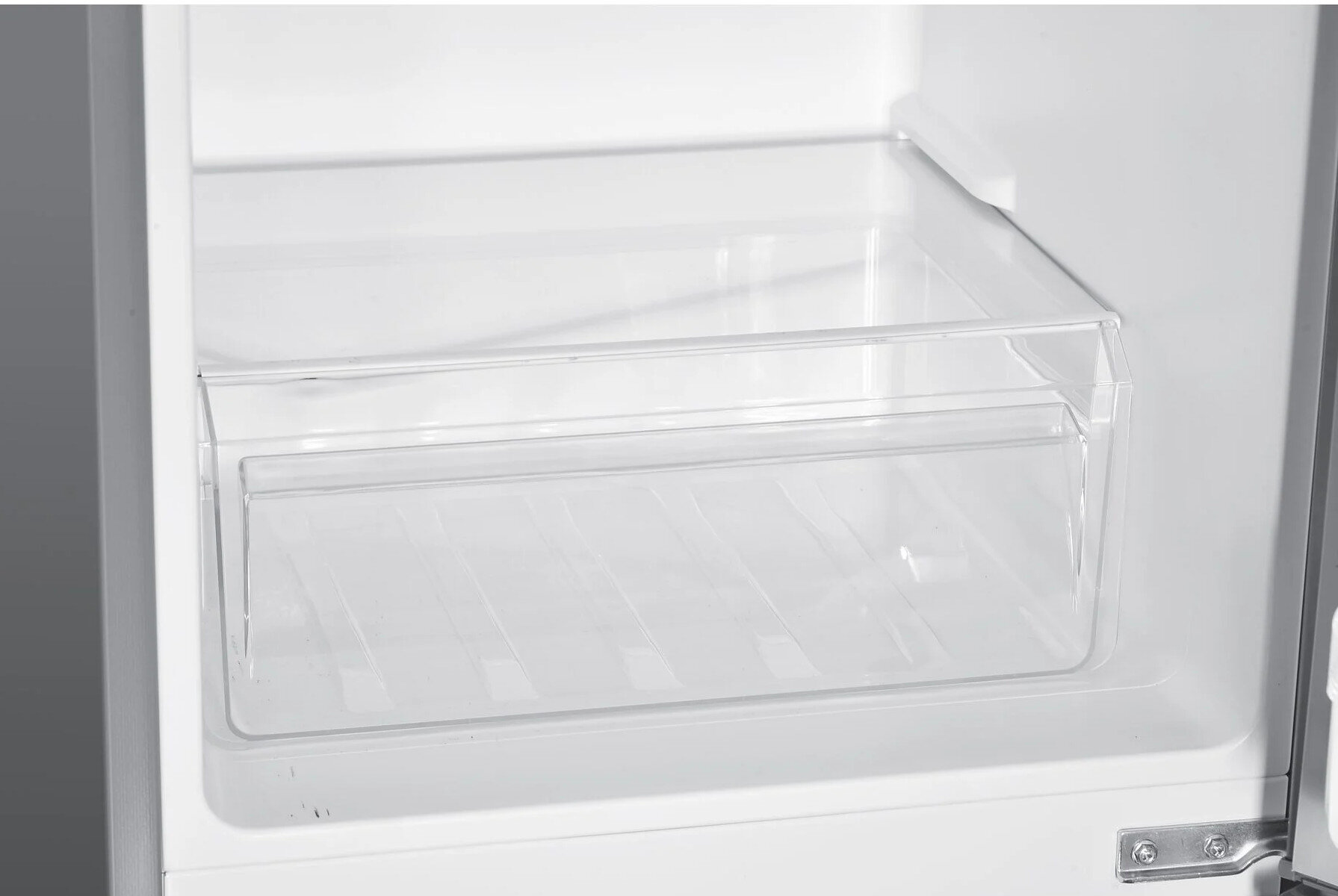 Wnętrze lodówki. Jest szuflada z przezroczystym plastikowym pojemnikiem.