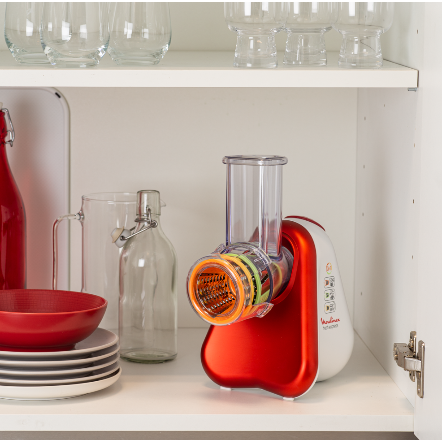 Red and white Moulinex food processor on a shelf with glasses and jars.