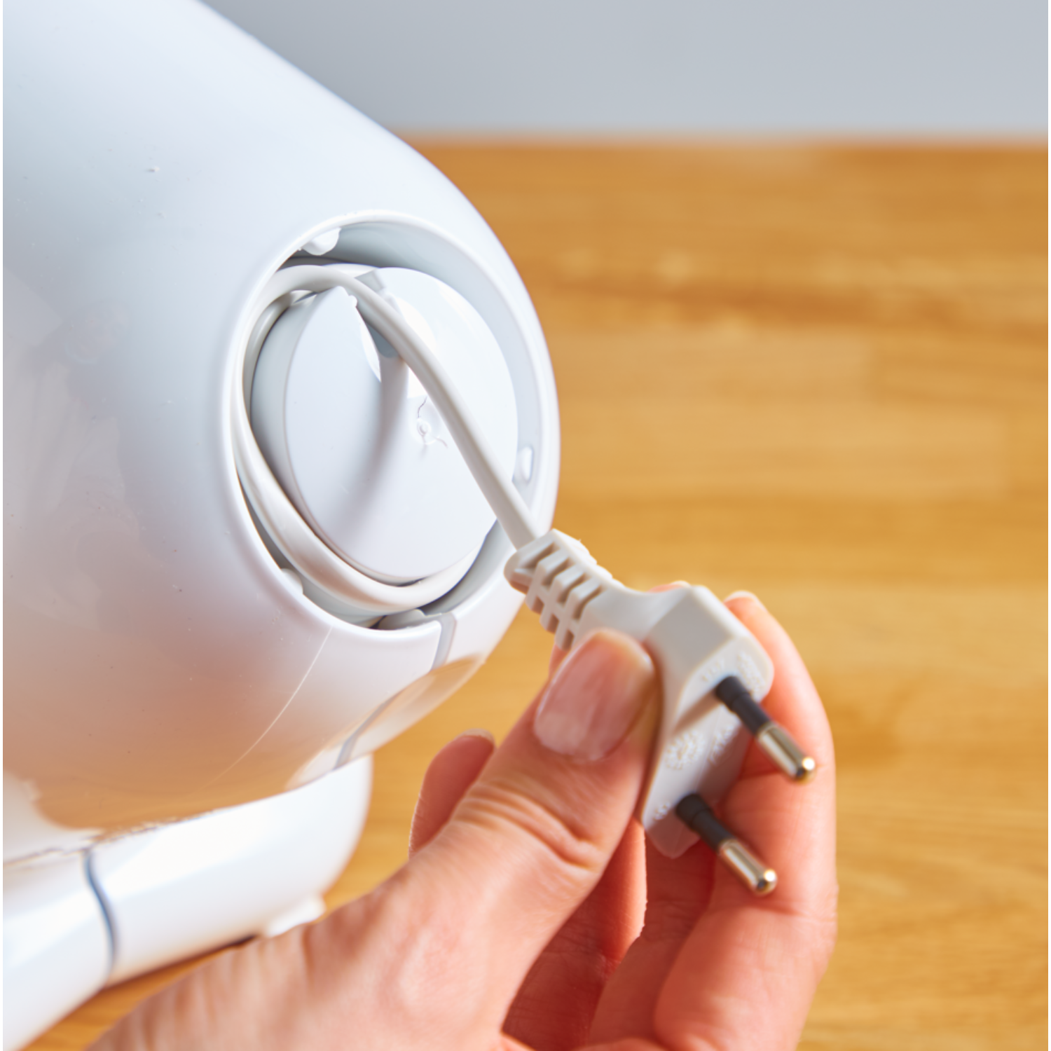 A hand holding a white plug, preparing to plug it in.