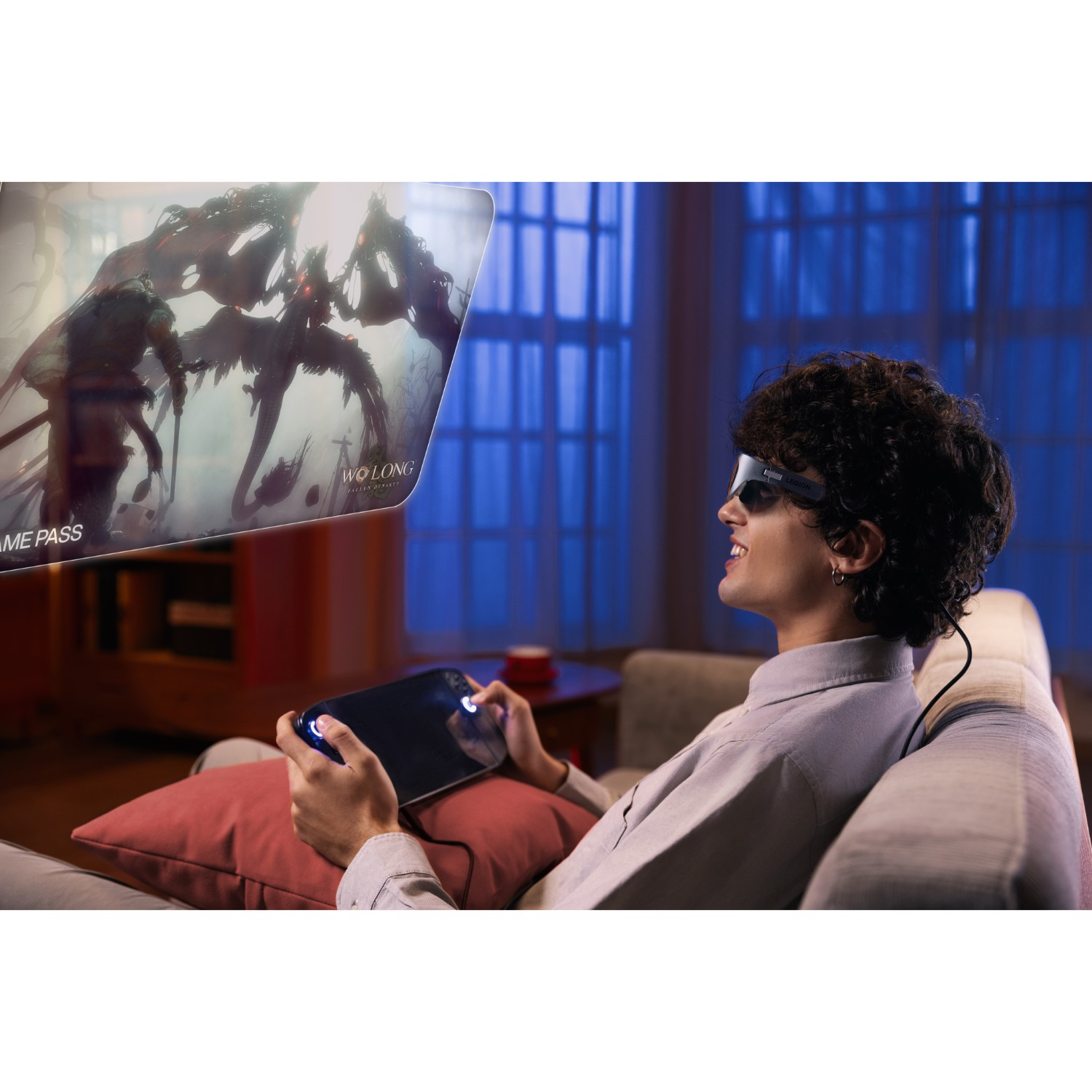 Un homme portant des lunettes joue à un jeu sur une console portable assis sur un canapé.