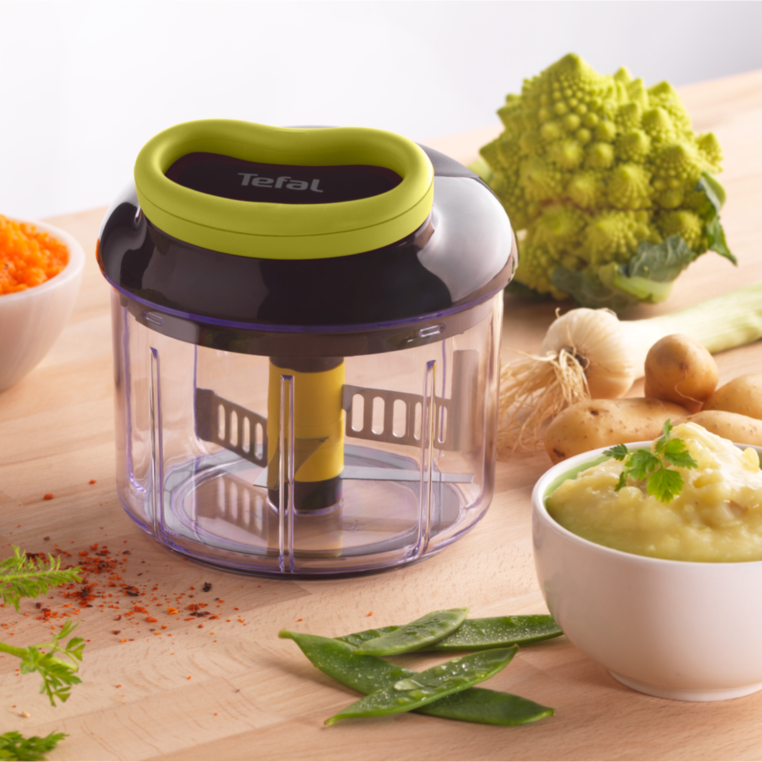 A food processor with food items around it, on a wooden surface.