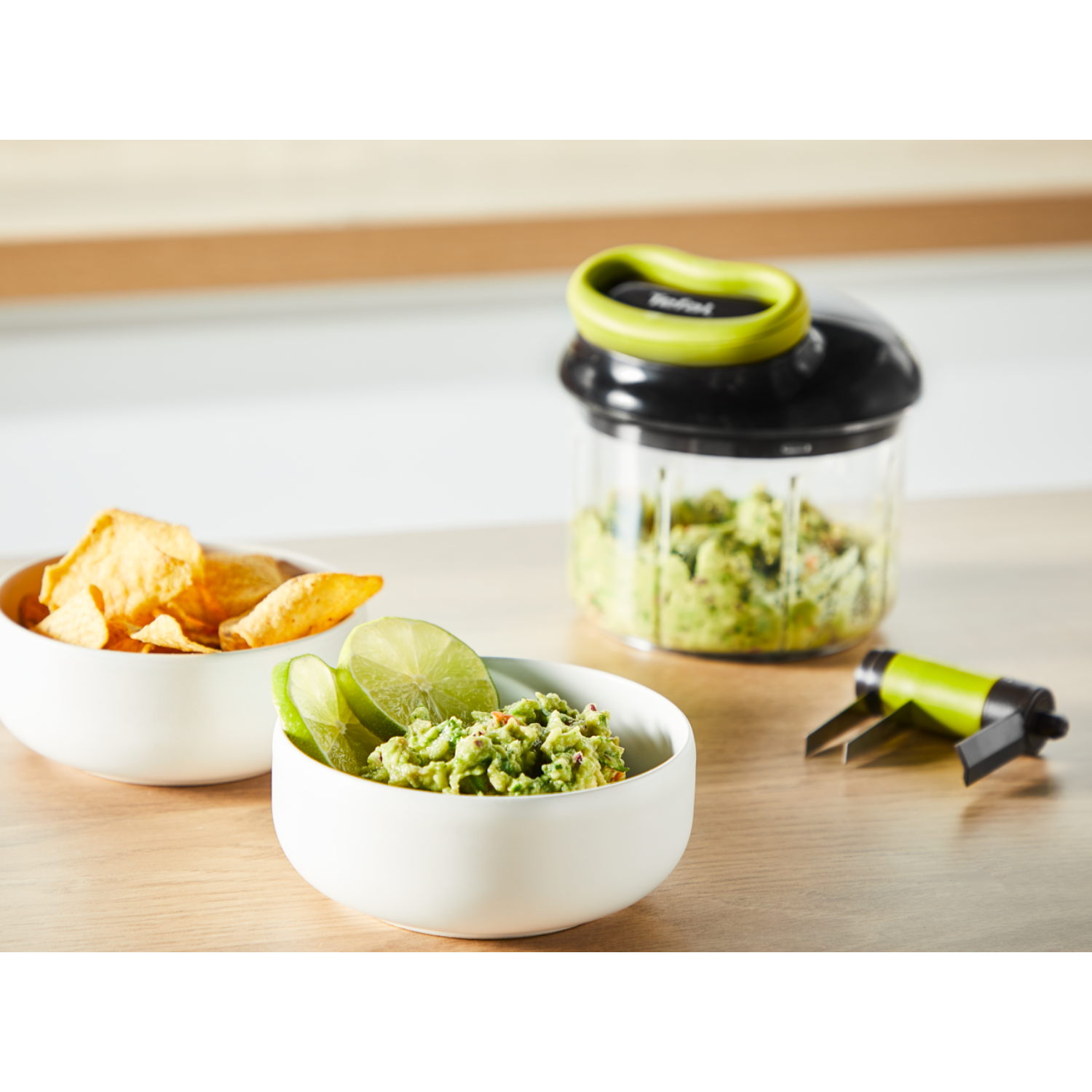 A bowl of guacamole, chips, and a Tefal manual food chopper with guacamole inside.