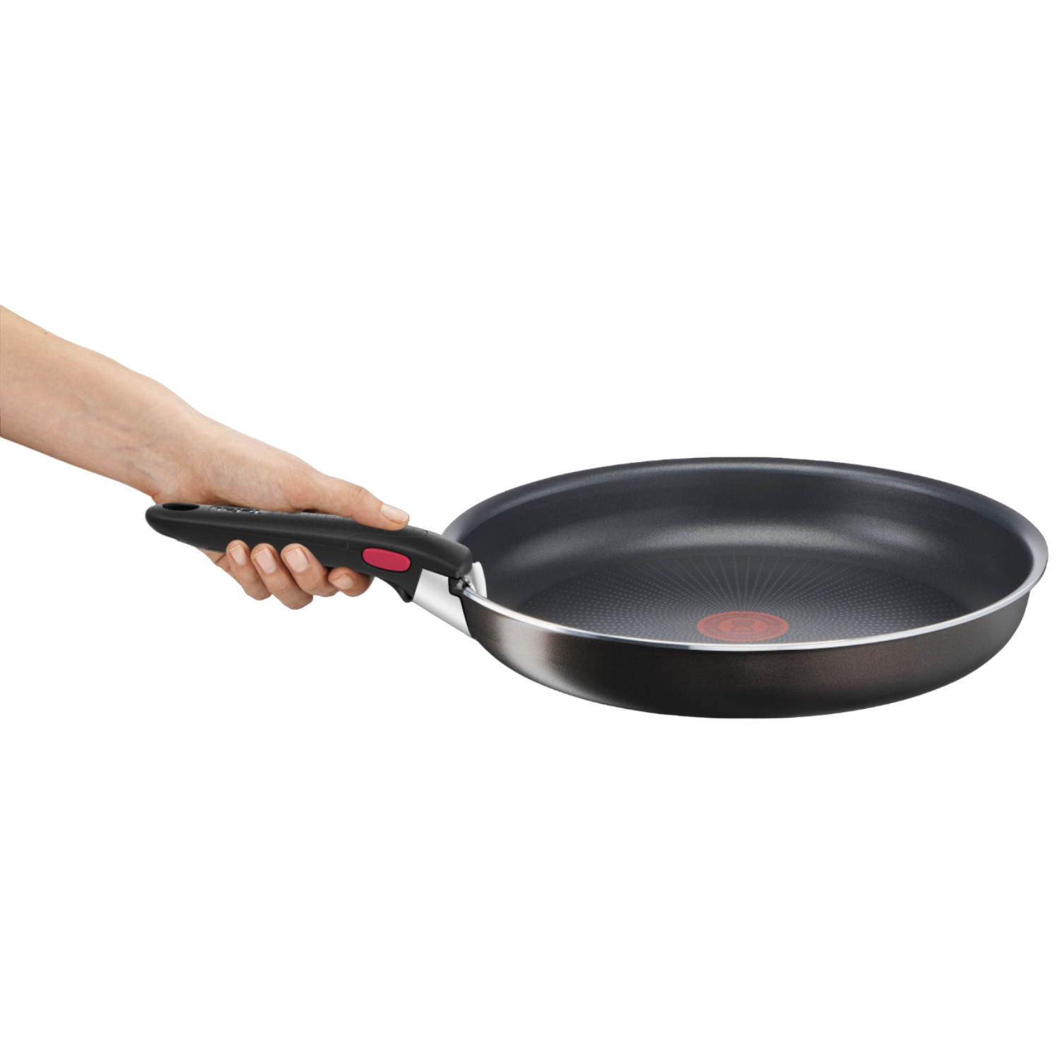 Une main tient une poêle noire avec manche rouge et bord argenté. Fond noir.
