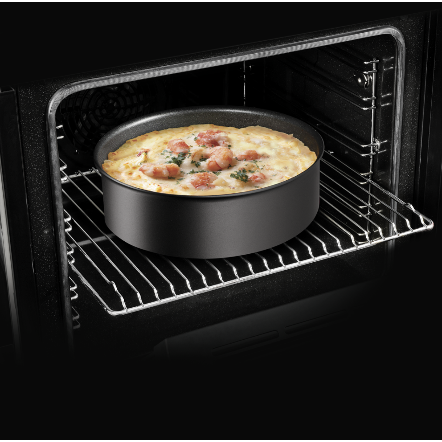 Pizza dans un moule noir à l'intérieur d'un four. Le four est sombre avec une grille métallique. La pizza est visible.