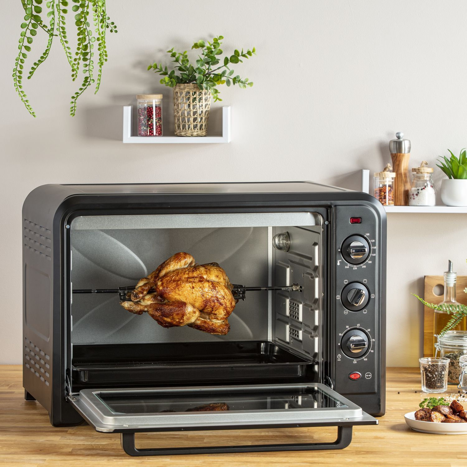 A black oven with a rotisserie chicken inside and a door open.