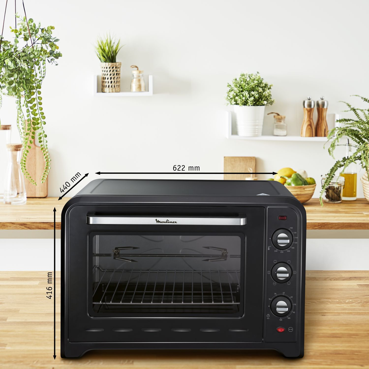 Black Moulinex oven with dials, rack, and measurements (440x622x416mm) on a wooden counter.