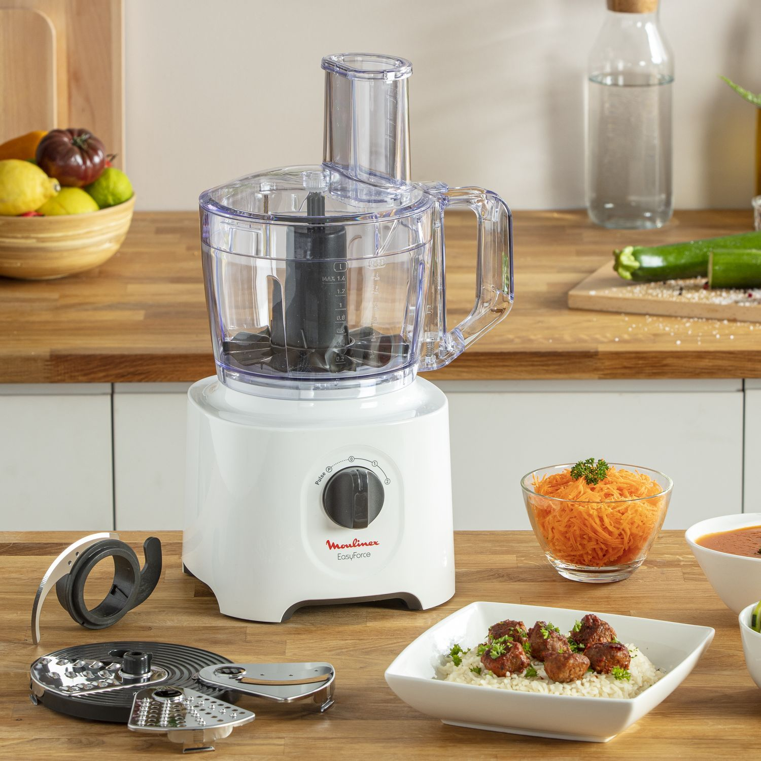 Robot culinaire blanc sur surface en bois avec ingrédients et accessoires.