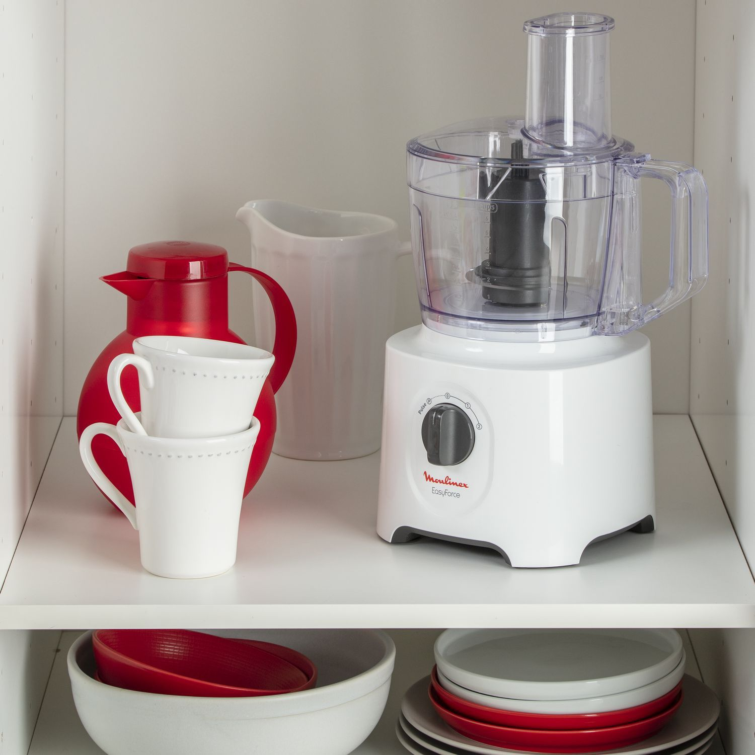Robot culinaire blanc et articles rouges sur une étagère. Le robot est au centre, avec pichet et tasses rouges.