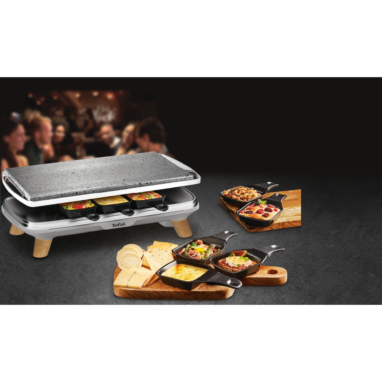 Raclette grill met eten. Mensen wazig op de achtergrond. Kaas, groenten en ingrediënten zichtbaar.