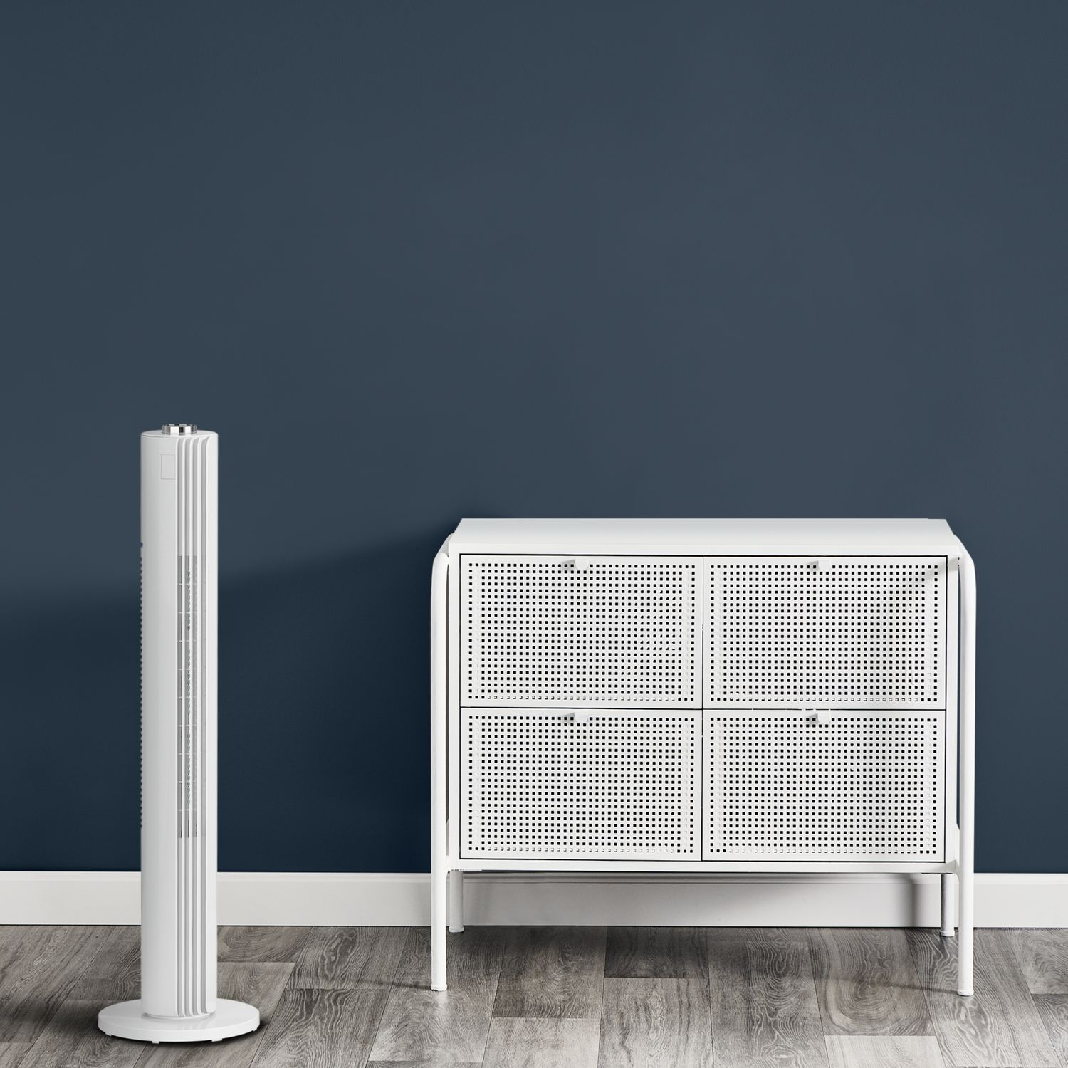 Een witte ventilator en kast staan tegen een donkerblauwe muur, op een houten vloer.