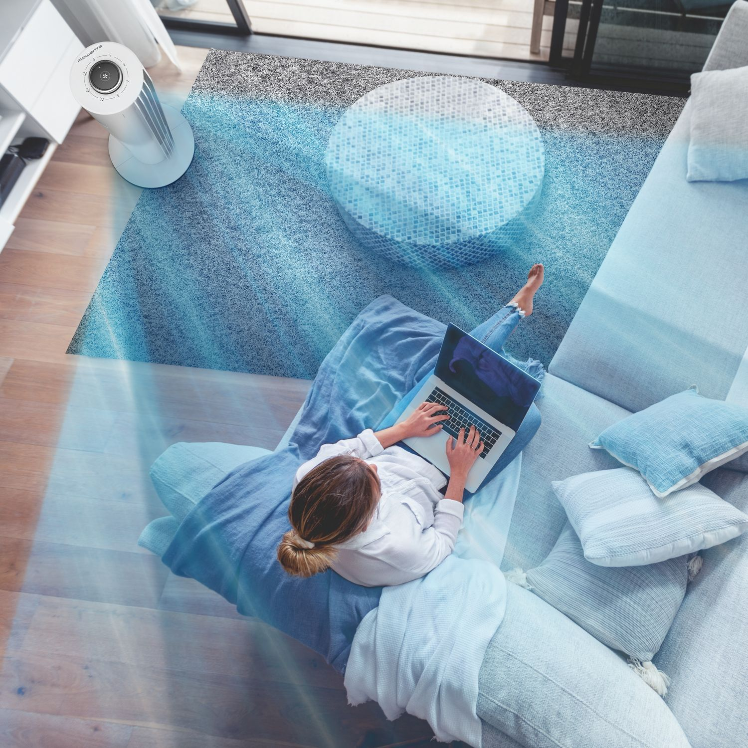 Vrouw gebruikt laptop op de bank. Ventilator blaast lucht in de kamer. Bovenaanzicht van de scène.