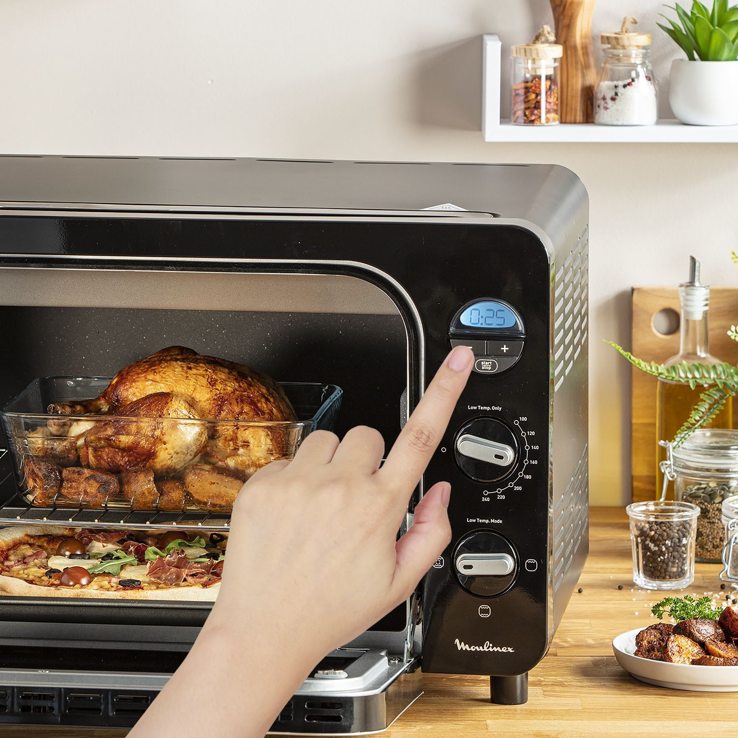De hand van een persoon die de timer aanpast op een zwarte Moulinex oven met voedsel erin. Houten oppervlak.