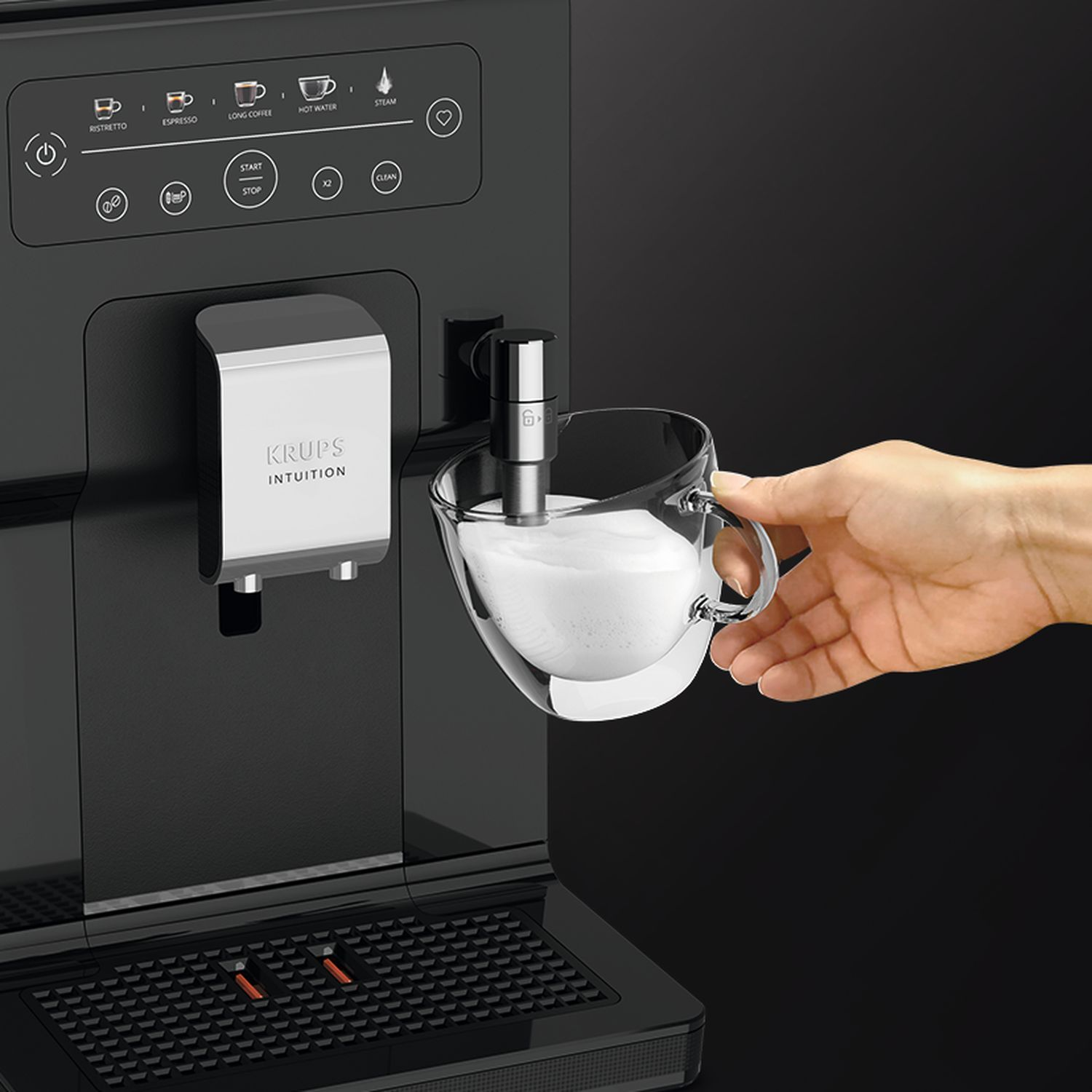 Een koffiemachine met een hand die een glazen kop vol melkschuim vasthoudt.