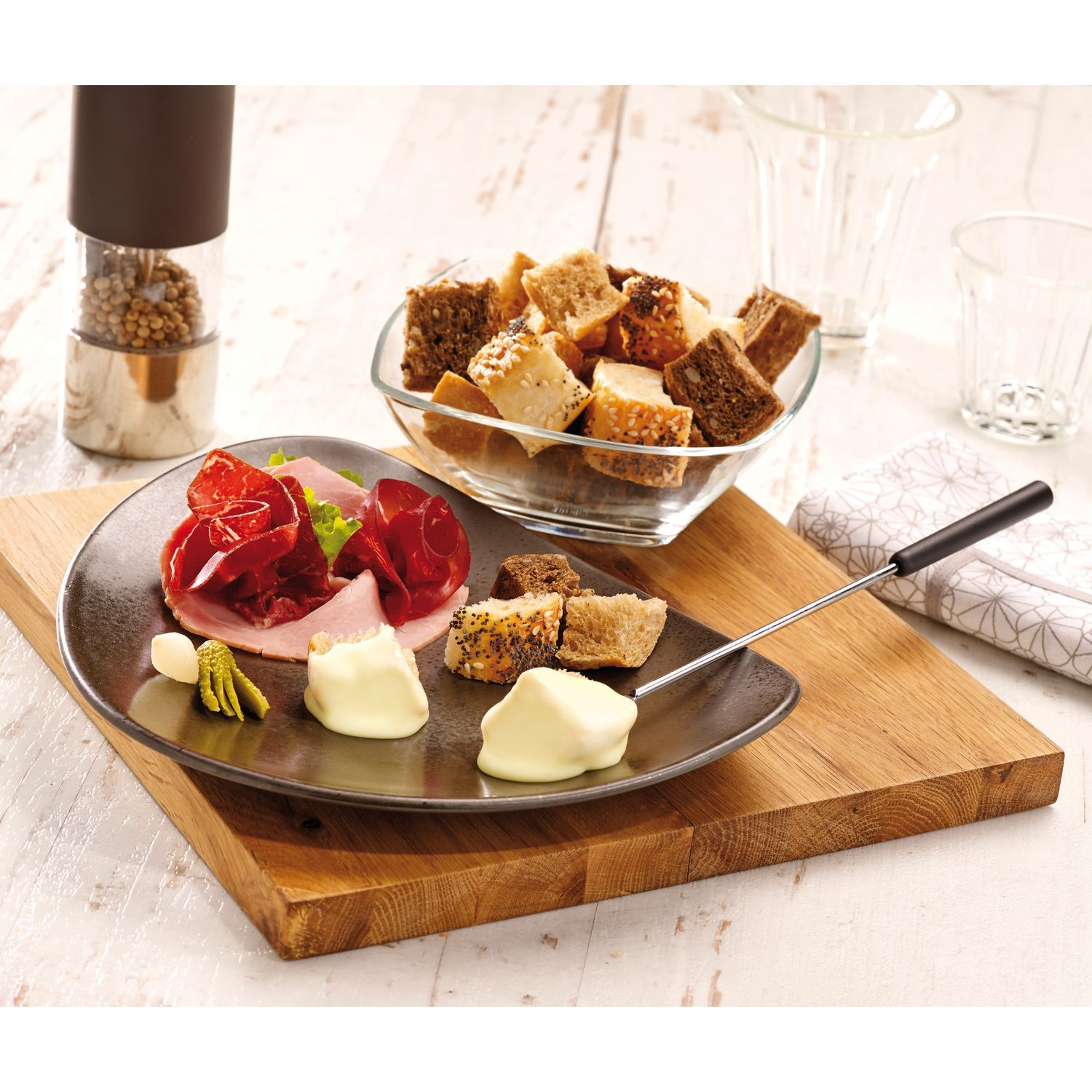 Planche en bois avec nourriture : pain, fromage, jambon et un moulin à poivre. Fond blanc.