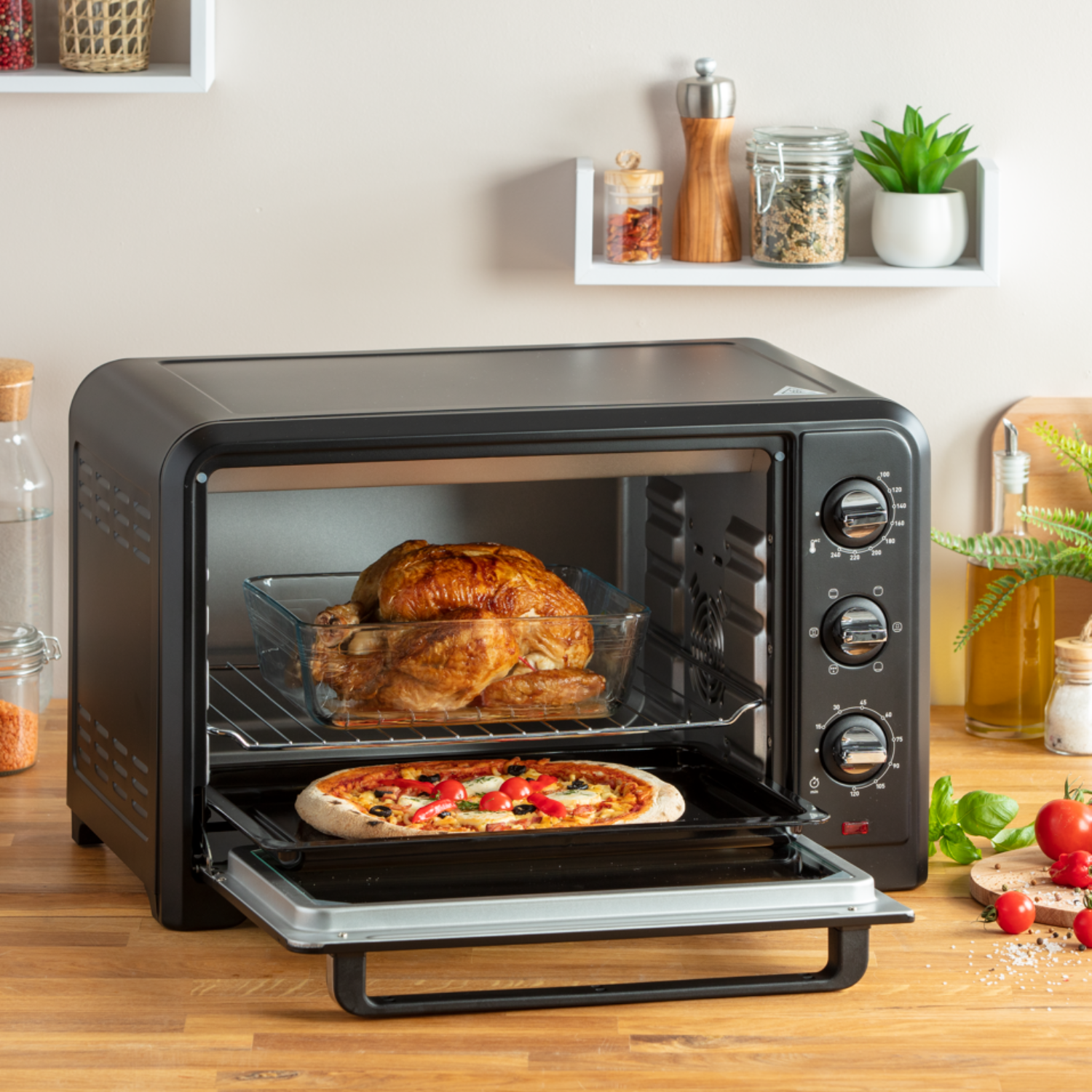 Een zwarte oven met een gebraden kip en pizza erin, op een houten oppervlak, met open deur.