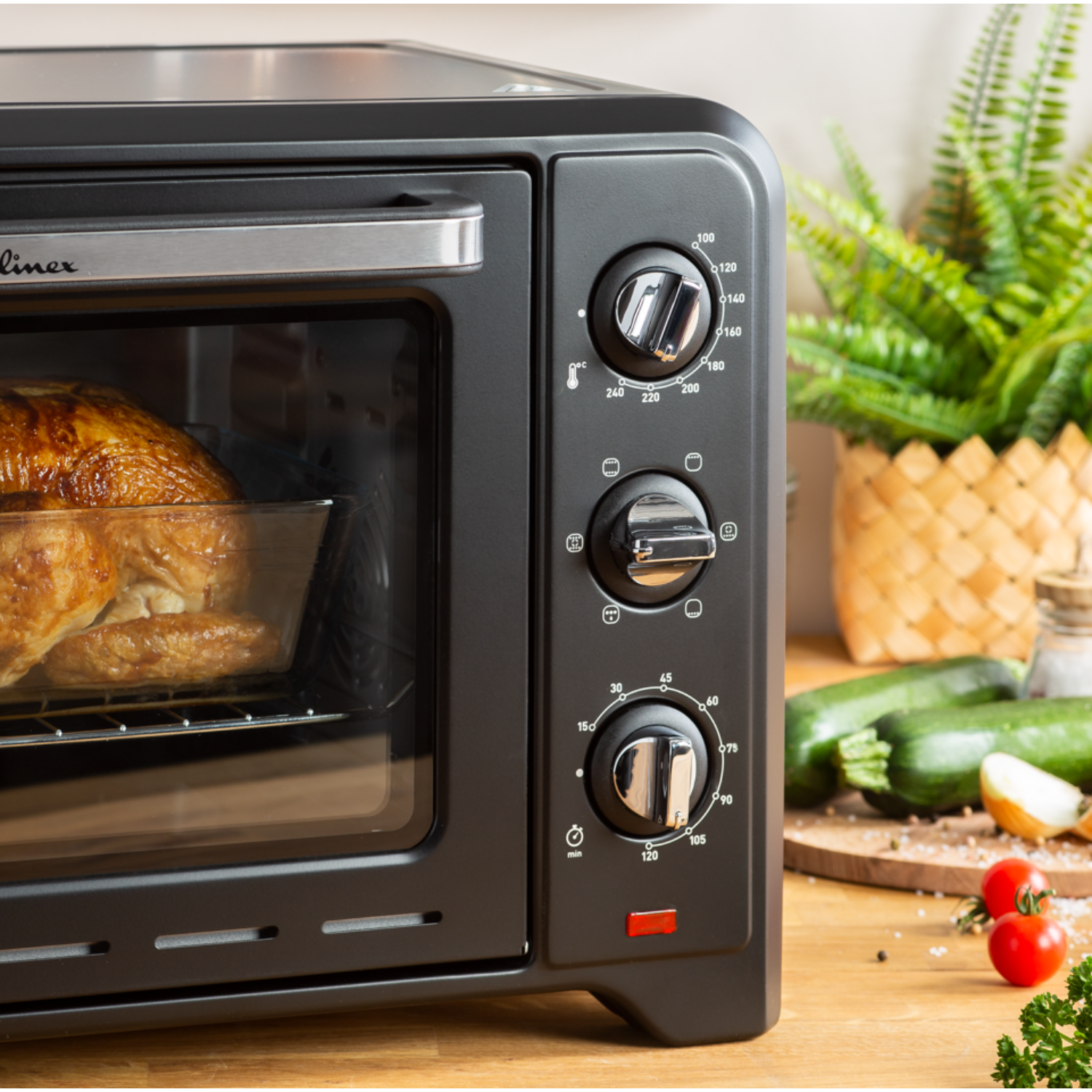 Zwarte oven met gebraden kip in glazen schaal. Groenten en knoppen zichtbaar. Keukenomgeving. Houten oppervlak.