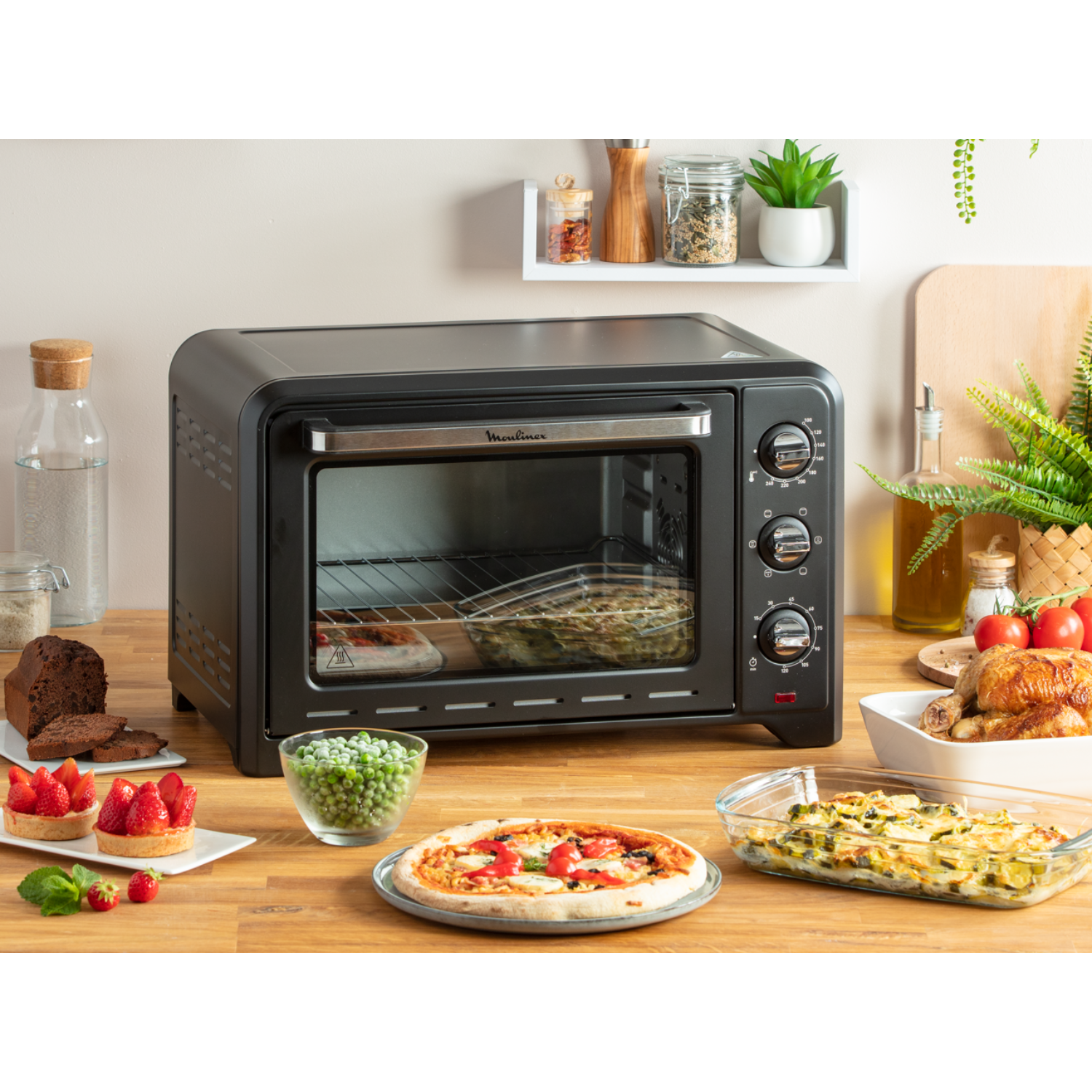 Zwarte oven met eten erin en op tafel: pizza, taarten, erwten en ovenschotel.