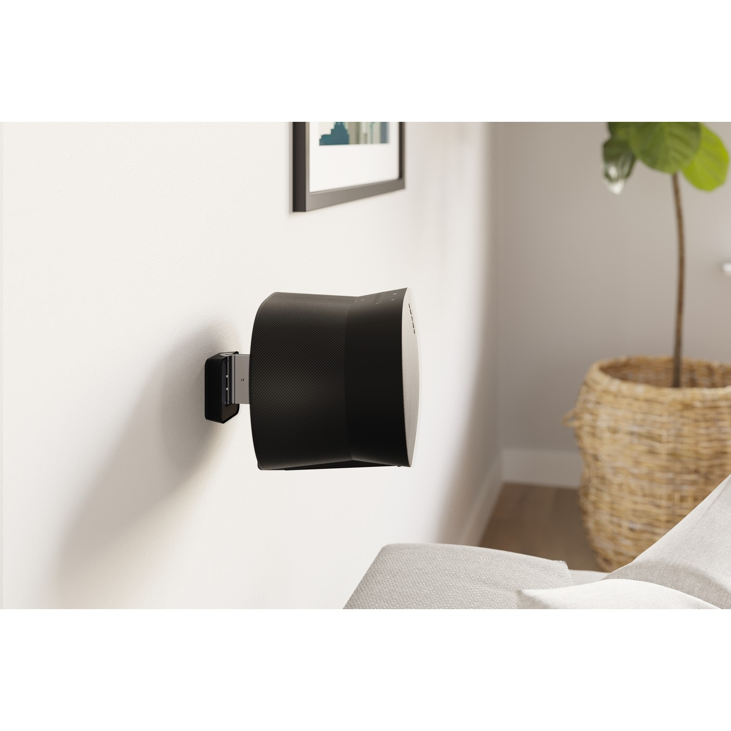 A black speaker is mounted on a wall. A picture and plant are in view.