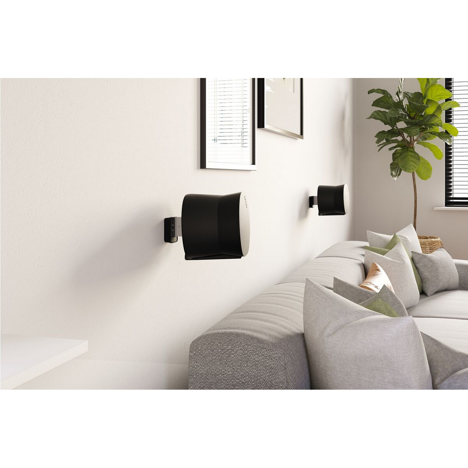 Two black speakers mounted on a white wall above a gray couch. A green plant is on the right.